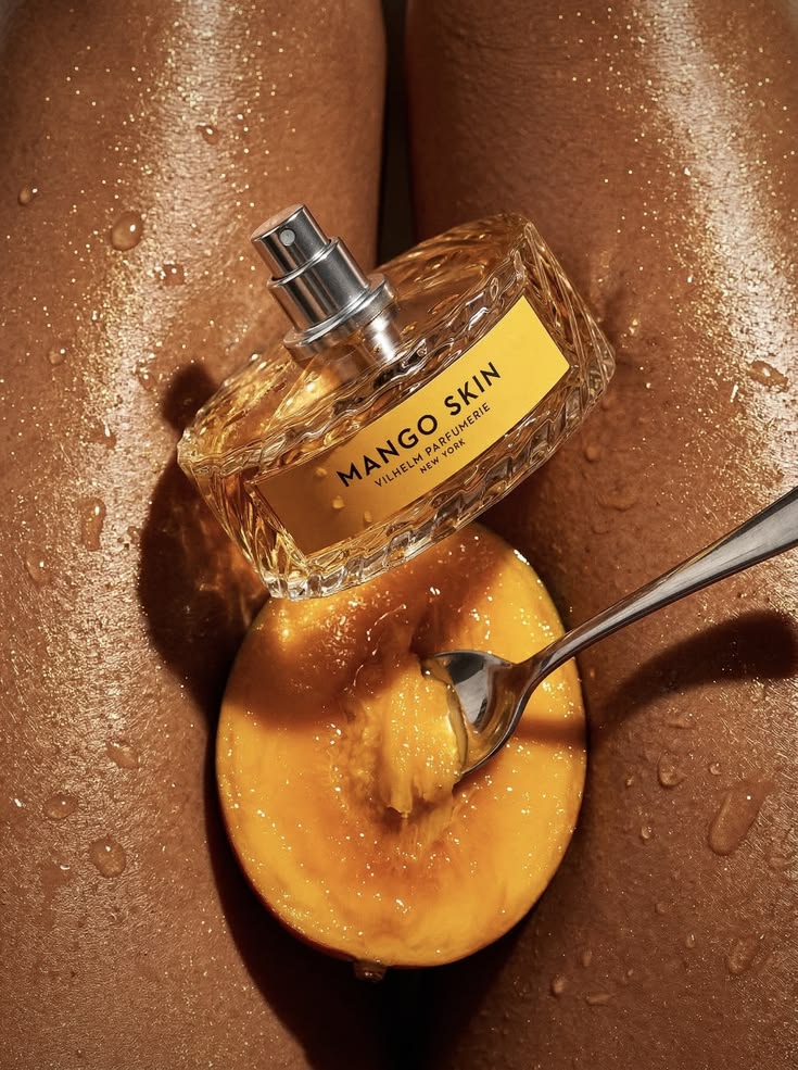 Parfum Mango Skin de Vilhelm Parfumerie posé sur une demi-mangue, mise en scène d'un produit au milieu de ses ingrédients