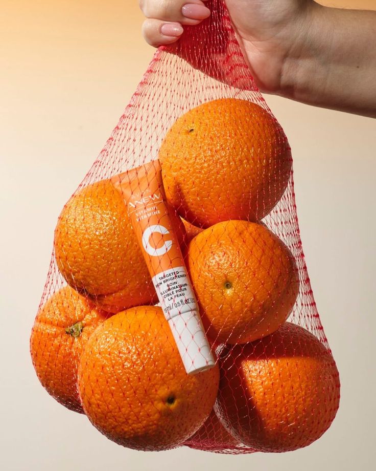 Main tenant un filet d'oranges avec un tube de soin Anew à la vitamine C