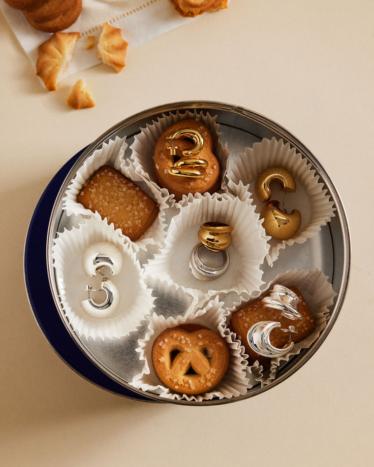 Boucles d'oreilles en or et argent présentées dans une boîte à biscuits, dans des caissettes en papier