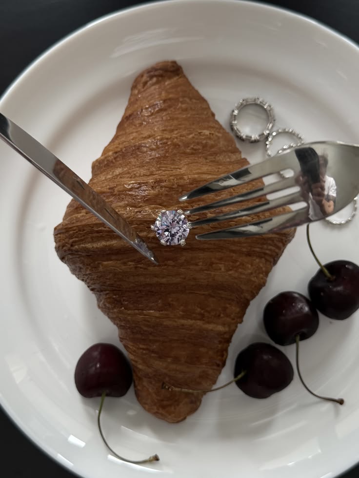 Bague à diamant posée sur un croissant, avec couteau, fourchette et cerises