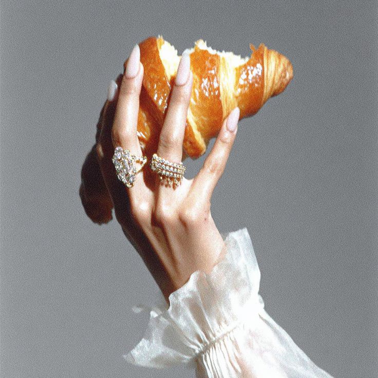 Main ornée de bagues en diamants tenant un croissant croqué