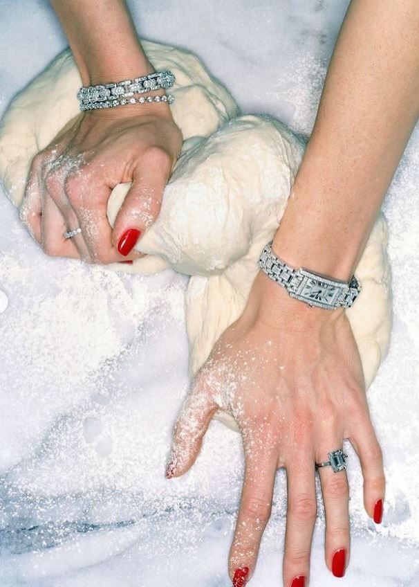 Mains couvertes de farine qui pétrissent une pâte, avec bracelets et bagues en diamants