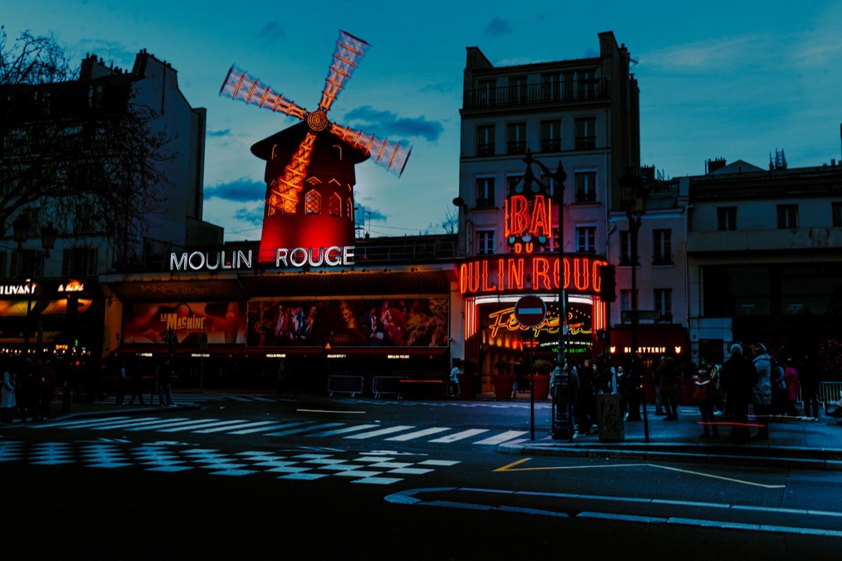 Façade du Moulin Rouge et son moulin rouge illuminé à la nuit tombée, lieu de soirée à Paris